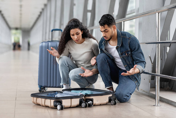 Stres mladý arabský pár mají problémy se zavazadly na letišti, frustrovaný středovýchodní manželé při pohledu na otevřený kufr, muž a žena trpí problémy po obdržení zavazadel v terminálu - Fotografie, Obrázek