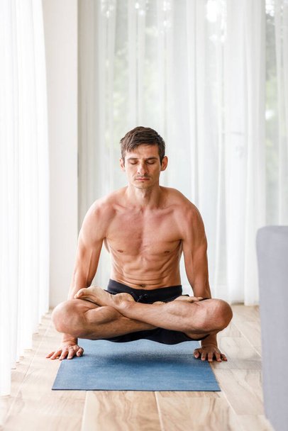 Young strong man doing yoga meditation breathing in hand standing routine in the morning. Full lotus pose in lolasana image - Fotografie, Obrázek