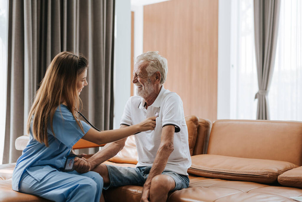 Een jonge verpleegster die bejaarde man thuis verzorgt. Aziatische verpleegster helpt oudere man thuis. Gezondheidszorg. - Foto, afbeelding