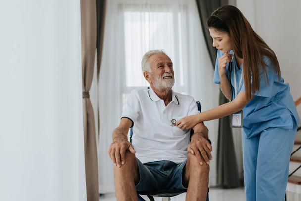 Young asian nurse helping senior man at home. Elderly man sitting on wheelchair and talking with young docter in house. Senior health care. - Foto, imagen