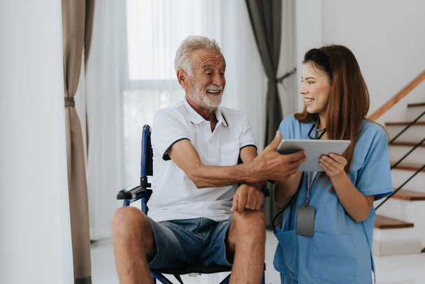 Infirmière asiatique et homme âgé regardant dossier médical sur tablette numérique à la maison. Vieil homme et infirmière utilisant tablette numérique ensemble pour regarder le plan de santé. Soins aux aînés - Photo, image