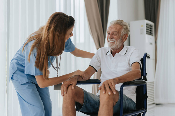 Joven enfermera asiática ayudando a un hombre mayor en casa. Un anciano sentado en silla de ruedas y hablando con un joven médico en casa. Asistencia sanitaria para personas mayores. - Foto, Imagen