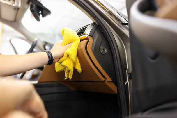 Κοντινό πλάνο του αρσενικού χέρι καθαρισμού εσωτερικό του οχήματος, καθαρότερο πλένει το αυτοκίνητο δερμάτινο σαλόνι. Υπηρεσίες καθαρισμού, ή αυτο-service πλύσιμο αυτοκινήτων, αφαίρεση της έννοιας της σκόνης - Φωτογραφία, εικόνα