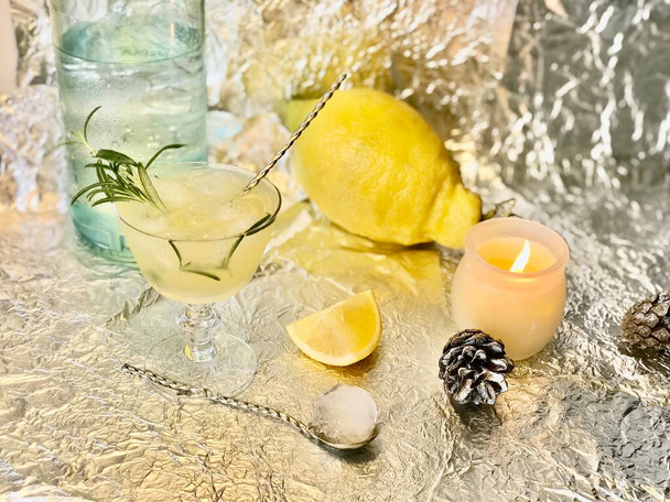 Koude citroendrank waarin men wat alcohol kan toevoegen met ijsblokjes en munt op stalen ondergrond met kaarsen - Foto, afbeelding
