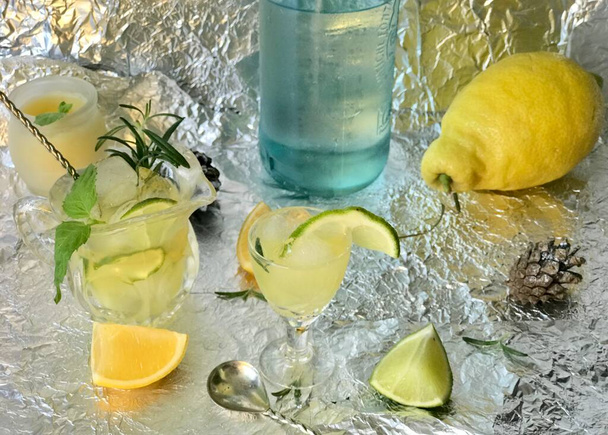 Cold lemon drink into which one can add some alcohol with ice cubes and mint on steel background with candles - Photo, Image