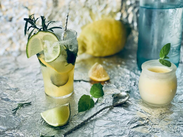 Cold lemon drink into which one can add some alcohol with ice cubes and mint on steel background with candles - Foto, Imagen