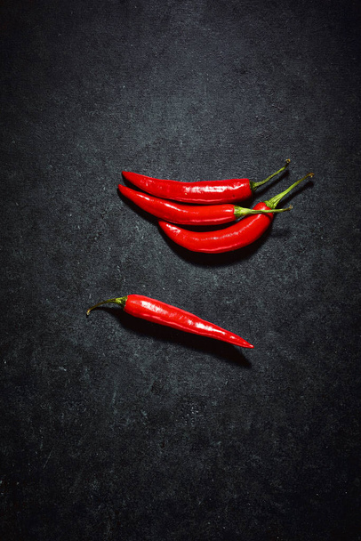 Red chilli peppers over dark background. Top down shot of glossy vegetable reflecting light. Spicy ingredients in kitchen. - Photo, image