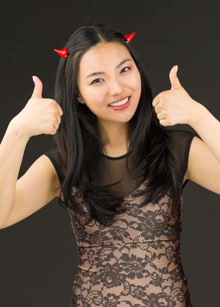 Asiática joven mujer vestida como un diablo con mostrar el pulgar hacia arriba signo con ambas manos
 - Foto, imagen