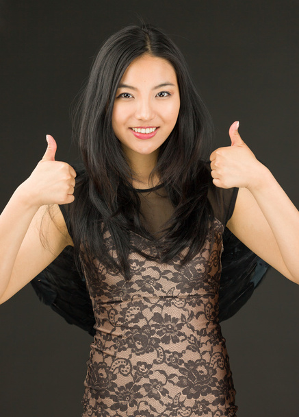 Aasialainen nuori nainen pukeutunut musta enkeli näyttää peukalo ylös merkki molemmin käsin
 - Valokuva, kuva