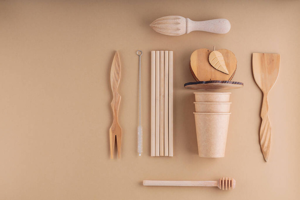 Wooden cutlery and paper disposable cups on a beige background. Wooden utensils, bamboo straws and cleaning brush. Sustainable or eco-friendly lifestyle. Plastic free concept - Fotó, kép