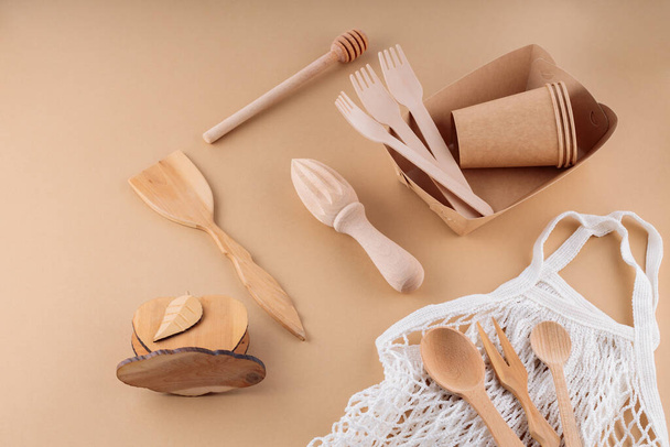 Eco-friendly kitchen utensils, paper disposable tableware and mesh bag. Wooden cutlery and shopping bag on a beige background. Sustainable lifestyle. Zero waste concept - Foto, Bild