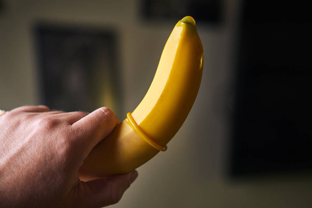 黄色のコンドームと黄色のバナナは屋内で男性の手を保持 - 写真・画像