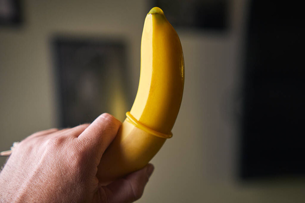 Yellow Condom and yellow banana holding a male hand indoors - Photo, Image