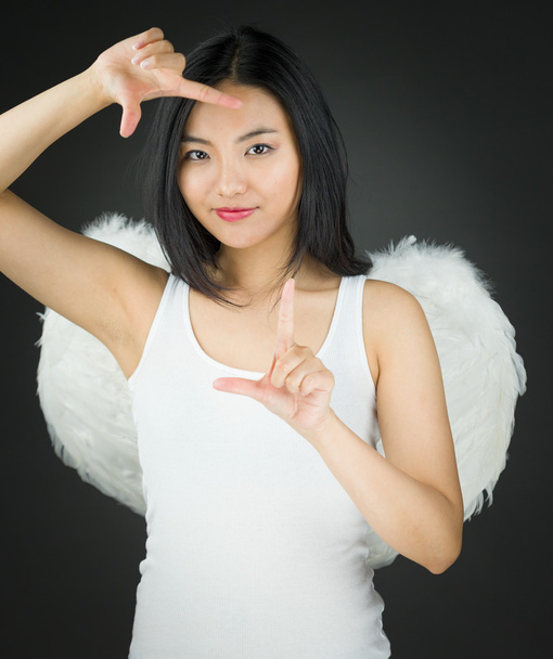 Asiático jovem mulher vestida como um anjo fazendo quadro com os dedos
 - Foto, Imagem