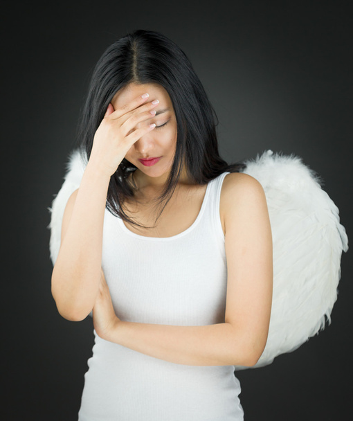 Расстроенная азиатская молодая женщина, одетая как ангел с головой в руках
 - Фото, изображение