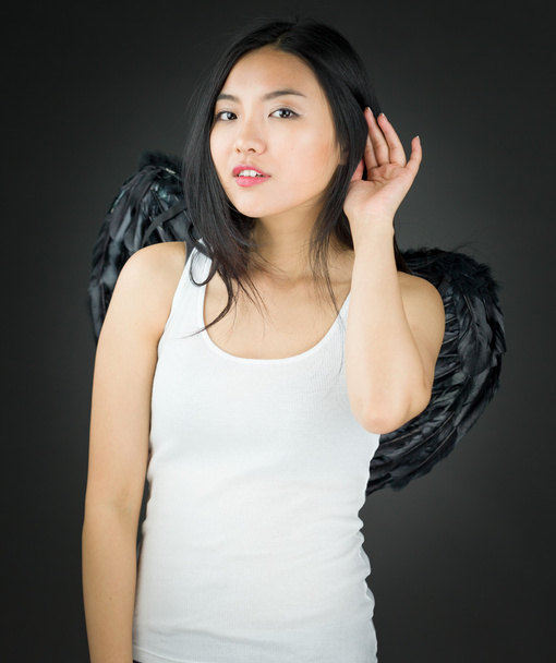 Aasialainen nuori nainen pukeutunut enkeli yrittää kuunnella tarkasti
 - Valokuva, kuva