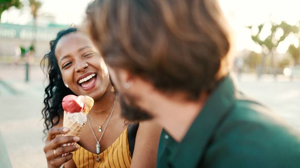 Closeup portrait of happy interracial couple eating ice cream in urban city background. Close-up of a man and woman tasting ice cream. Backlight - 写真・画像