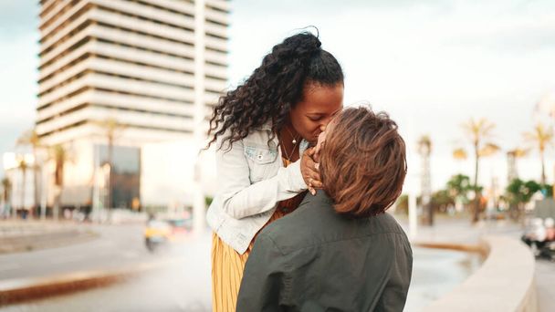 Close-up of an interracial couple in love. Man and woman hugging and kissing each other on urban city background - Foto, Imagem