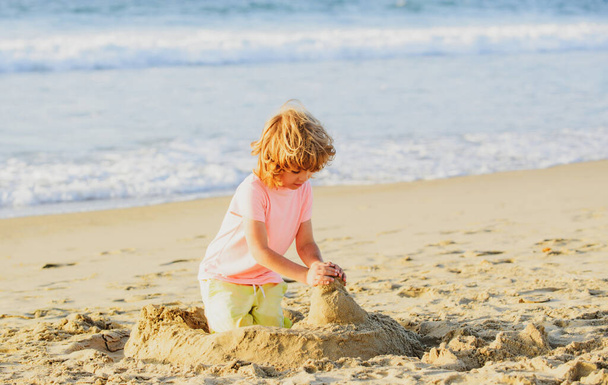 Boy playing on the beach on summer holidays. Children building a sandcastle at sea - Valokuva, kuva