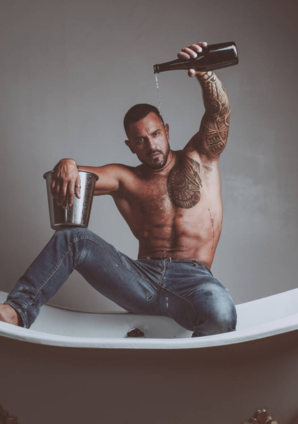 Luxury elite leisure. A concept of luxury life with champagne bottle. Brutal man with a bottle of champagne which pours into the bath. Luxury life. Attractive men with luxury elite alcohol - 写真・画像