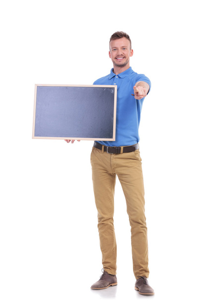 casual young man holds blackboard and points at you - Foto, imagen