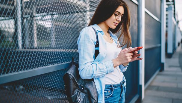 Millennial hipster girl in ottica occhiali lettura pubblicazione di rete utilizzando l'applicazione cellulare in città - Foto, immagini