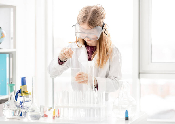 Girl doing scientific chemistry experiment wearing protection glasses. Schoolgirl with equipment and chemical liquids on school lesson - Fotoğraf, Görsel