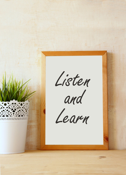 The phrase listen and learn written over white drawing board against rustic textured wall - Foto, Imagen