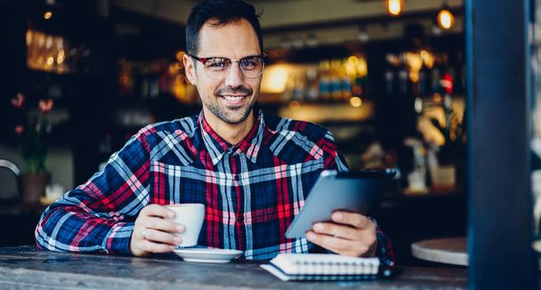 Portrait of smiling man looking at camera during coffee break for updating application on digital tablet - Fotó, kép