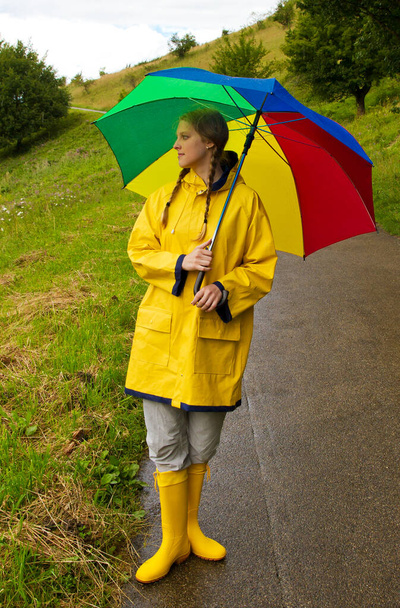 Νεαρή γυναίκα με ομπρέλα και κίτρινο αδιάβροχο στη βροχή - Φωτογραφία, εικόνα