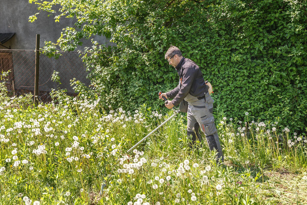A man mows the grass in the garden with a gasoline trimmer. He wore eye glasses to protect his eyes. Work in the garden in the spring. - Fotoğraf, Görsel