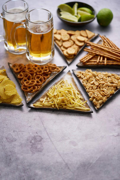 Alto angolo di deliziosi snack vari patatine fritte, bastoncini, arachidi sul tavolo con vetro di birra - Foto, immagini
