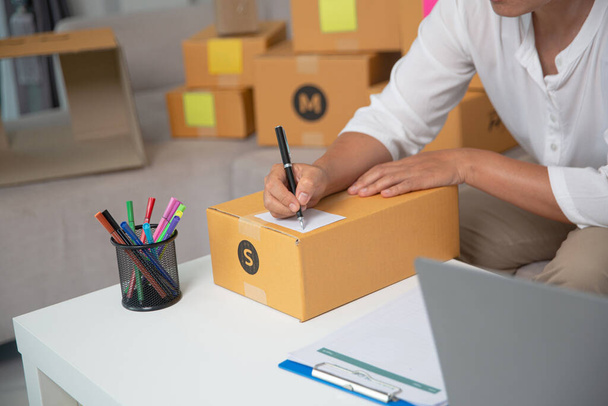Крупный план владельца бизнеса, рукопись на коробках с посылками для доставки продукции клиентам дома. - Фото, изображение