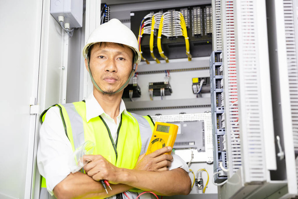 handsome electrical engineer arms crossed and current of power electric line in electrical cabinet control. - Photo, Image