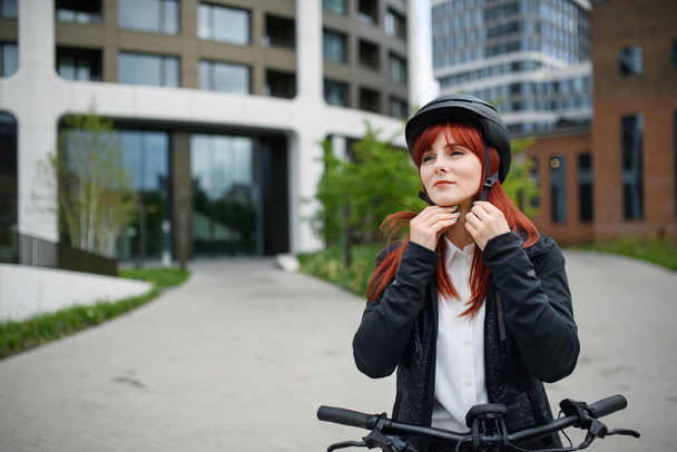 A portrait of businesswoman commuter on the way to work putting on cycling helmet, sustainable lifestyle concept. - Foto, Imagen