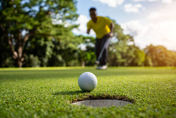 Golfista dává míček na zelený golf, čočka září při západu slunce večerního času. Golfista akce vyhrát po dlouhé uvedení golfového míčku do jamky. - Fotografie, Obrázek