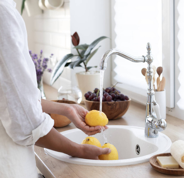 Девушка моет лимоны на кухне. Делаю освежающий летний напиток. Концепция здорового питания. - Фото, изображение