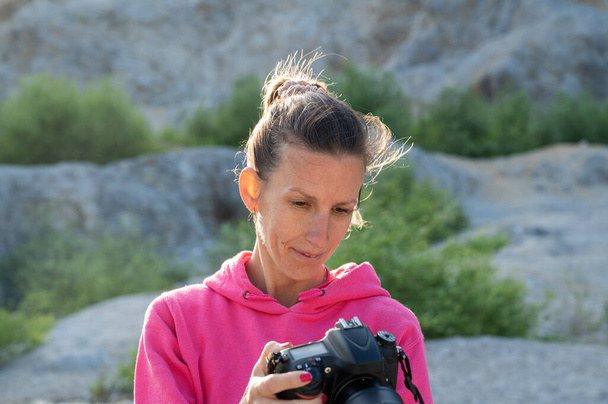 Молодая женщина-фотограф проверяет настройки камеры перед фотосессией в заброшенном карьере. - Фото, изображение
