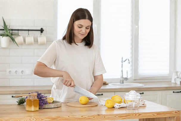 Young woman cutting lemon on wooden board. Preparation of fresh emonade. Lavender and lemon - Foto, immagini