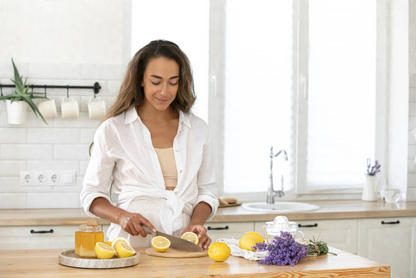 Young woman cutting lemon on wooden board. Preparation of fresh emonade. Lavender and lemon - Photo, Image