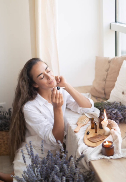 Using natural essential oil in a home spa ritual. A woman takes care of her skin and hair - Zdjęcie, obraz