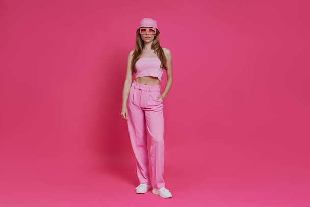 Full length of beautiful young woman in trendy clothing standing against pink background - Foto, Imagen