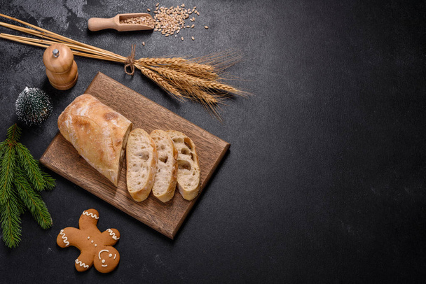 Francouzský bagetový chléb krájený na dřevěné řezací desce na tmavém betonovém pozadí. Příprava jídelního stolu - Fotografie, Obrázek