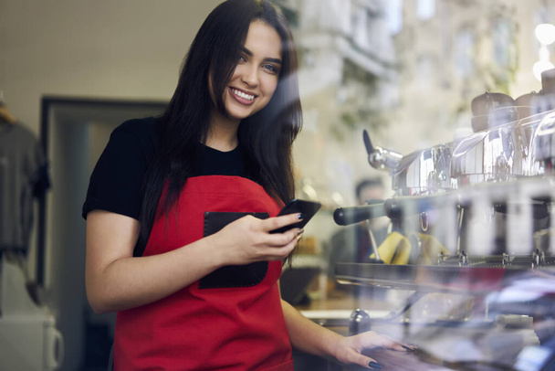 20s smiling female manager of coffee shop holding smartphone share content about job in blog - Photo, Image