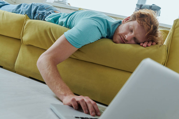 joven pelirroja se sentía dormido mientras se acostaba en el sofá y el uso de la computadora portátil - Foto, imagen
