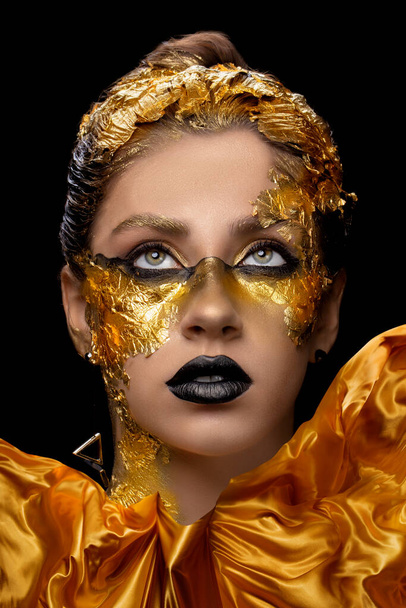 Divatművészet Arany bőr. Modell lány ünnepi arany csillogó fényes professzionális make-up. Arany ékszerek, bijouterie, kiegészítők. Gyönyörű arany fém test, fekete ajkak és bőr. - Fotó, kép