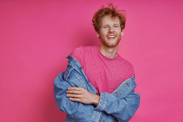 Handsome redhead man in denim clothing standing against pink background - Photo, image