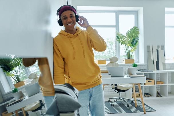 Happy multiracial man in headphones enjoying music while standing at home office - Photo, Image