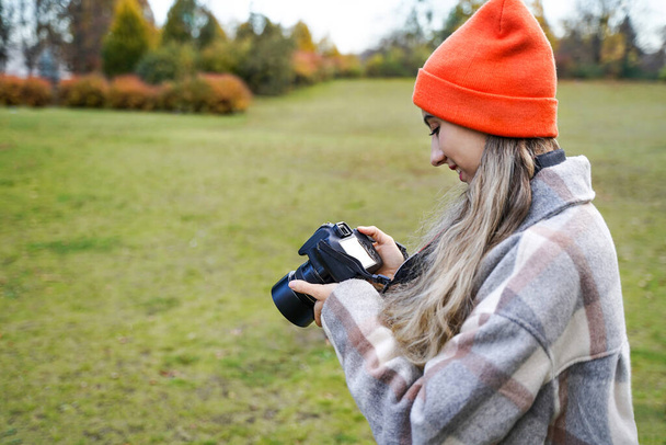 Chica con cámara se ve la foto. Mujer joven toma fotos en primavera al aire libre. Hobby, ocio - Foto, Imagen