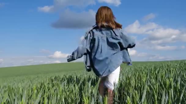 Happy teen girl in the countryside running across the field. Happy farmer girl on wheat field. The girl plays and runs on the tall green grass. The concept of freedom - Footage, Video